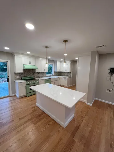 Open concept kitchen with white island, pendant lighting and hardwood floors renovated by Best In Class Renovations on Long Island
